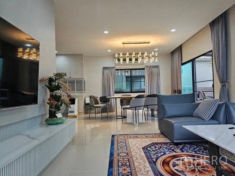 Detached House for rent or sale in Lam Luk Ka, Pathum Thani - Open-plan living and dining area with chandelier and gray sofas