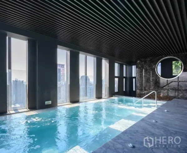 Condominium for rent in Khlong Toei, Bangkok - Indoor swimming pool with marble deck and skyline views through tall windows.