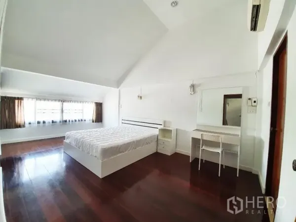 Detached House for rent in Phra Khanong, Bangkok - Bright bedroom with high ceiling, dark wood floors, large window, bed and vanity.