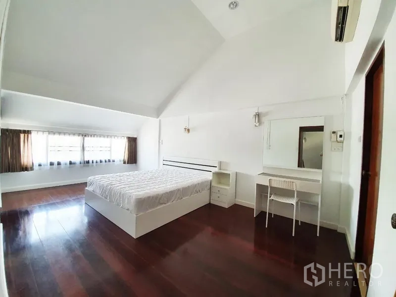 独立式住宅 出租在Phra Khanong, Bangkok - 高挑卧室，深色木地板，大窗采光，白墙，床与梳妆台，空调。