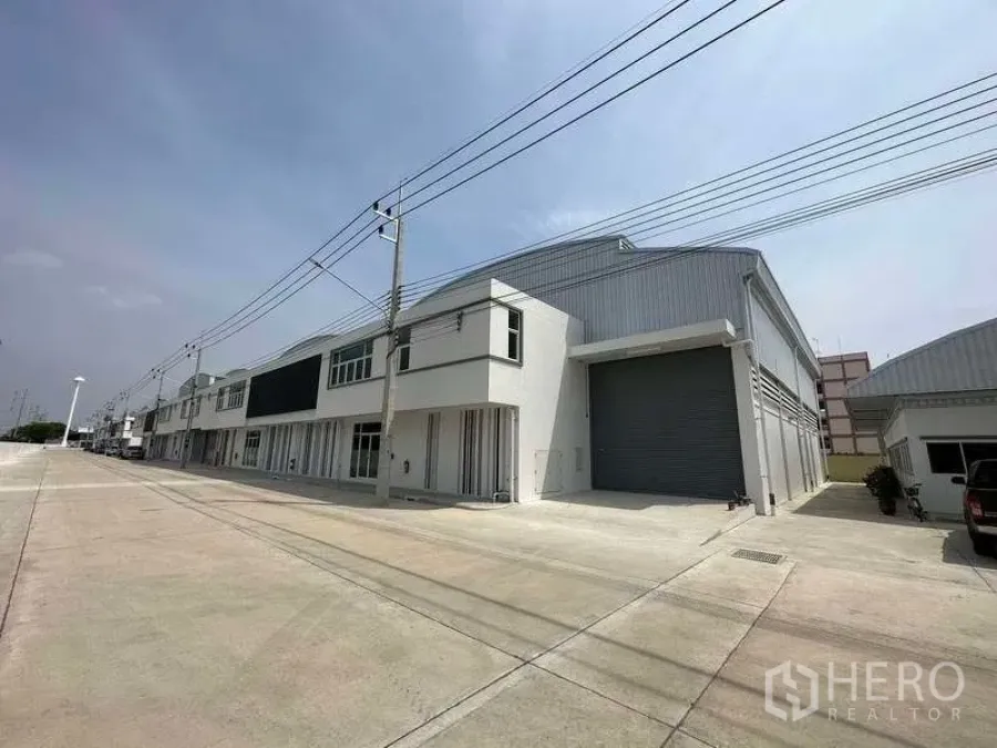Factory for rent in Khlong Luang, Pathum Thani - Street view of factory row with driveway leading to a large loading door.