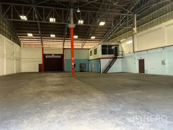 Warehouse for rent in Mueang Samut Prakan, Samut Prakan - Spacious warehouse interior with high ceiling, steel truss roof, polished concrete floor, and mezzanine office with staircase.