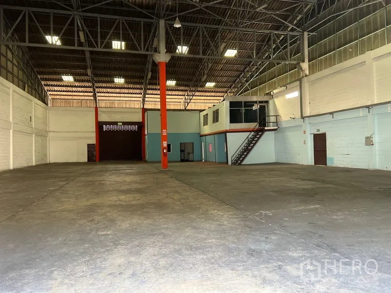 Warehouse for rent in Mueang Samut Prakan, Samut Prakan - Spacious warehouse interior with high ceiling, steel truss roof, polished concrete floor, and mezzanine office with staircase.