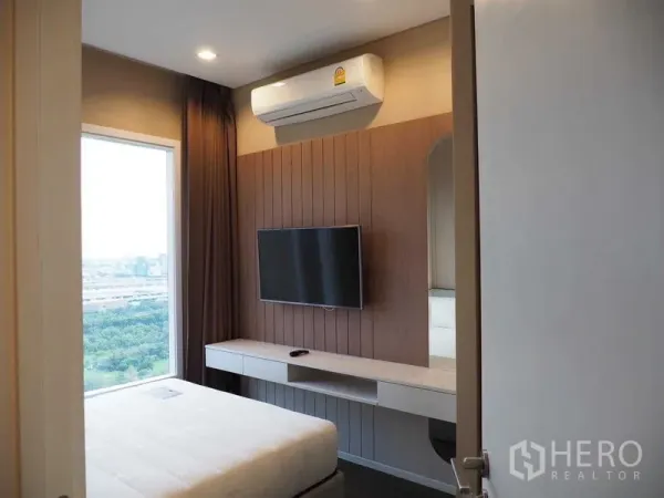 Condominium for rent in Chatuchak, Bangkok - Second bedroom featuring wall-mounted TV, built-in desk, air conditioning and a wide window outlook.