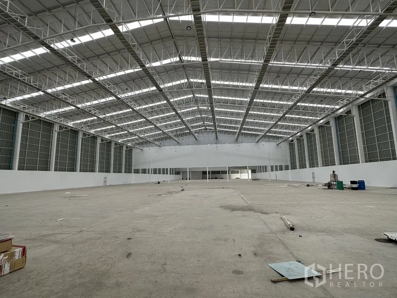 工厂 出租在Pathum Thani - 宽大的高标仓库大厅，钢桁架屋顶与通风玻璃砖窗。