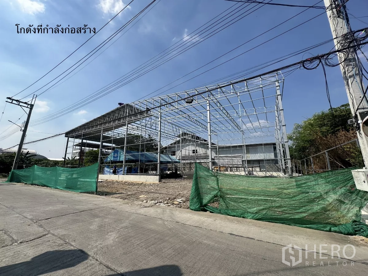 Warehouse for rent in Bang Kapi, Bangkok - Warehouse steel frame under construction along a local street with power lines and green safety netting.