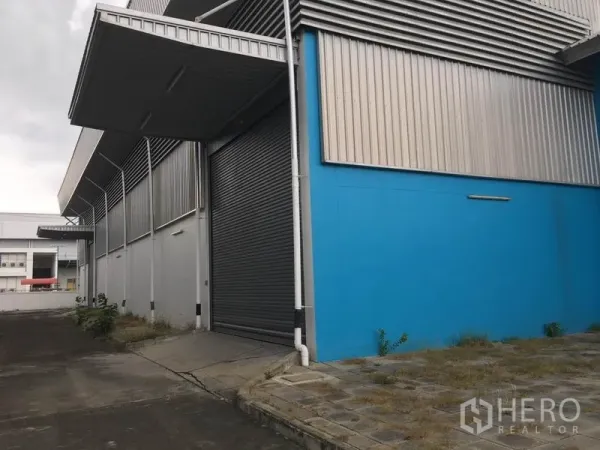 Factory for rent in Samut Prakan - Covered loading bay with a large roll-up shutter door and concrete ramp along the side of the factory.