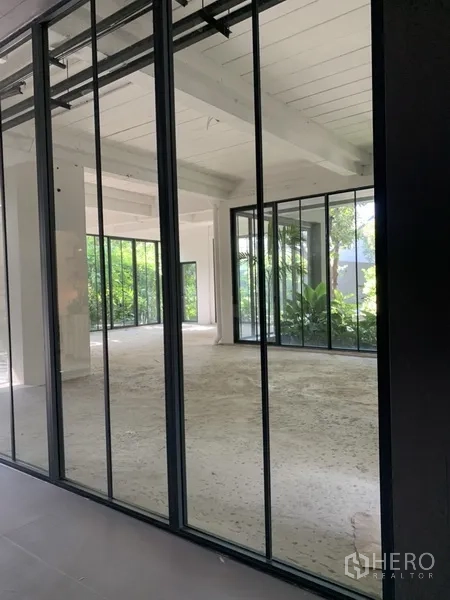 Office Space for rent in Khlong Toei, Bangkok - Shell office space with black-framed glass partitions and leafy garden views.