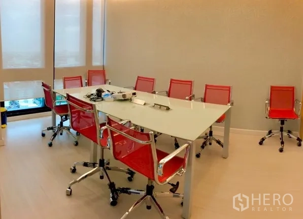 Office Space for rent in Bang Na, Bangkok - Conference room with a glass-top table and multiple red chairs, set beside shaded windows.
