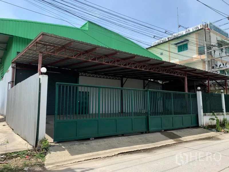 Factory for rent in Pathum Thani - Gated factory exterior with green roof, covered loading bay and sliding metal gate.