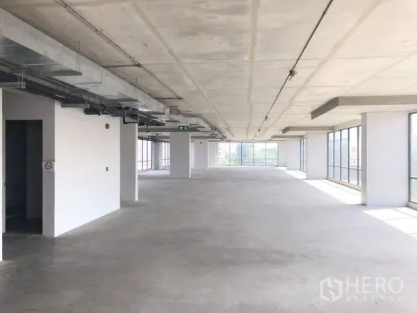 Office Space for rent in Suan Luang, Bangkok - Bright open workspace with pillars, expansive glazing on both sides, and emergency exit signage.