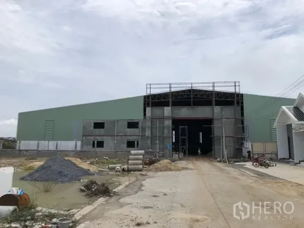 Warehouse for rent or sale in Sai Noi, Nonthaburi - Front exterior of a large steel-frame warehouse under construction with a wide entry and driveway.