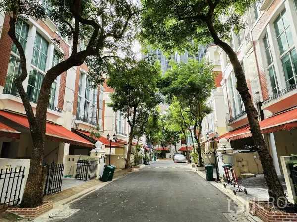 联排别墅 出租在Watthana, Bangkok - 社区内部林荫道路，两侧联排住宅配橙色遮阳篷与入户小门