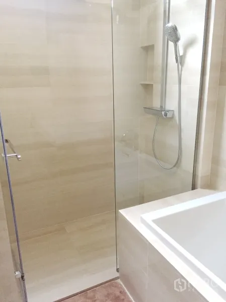 Condominium for rent in Watthana, Bangkok - Walk-in glass shower with rain showerhead and built-in shelves next to a bathtub.
