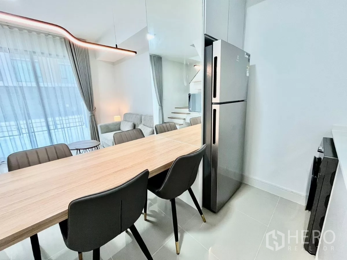 Townhouse for rent in Bang Phli, Samut Prakan - Bar-style dining table with sleek pendant light beside a stainless refrigerator and sheer-curtained window.