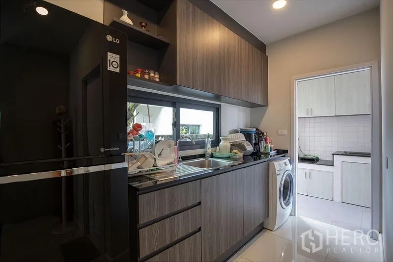 บ้าน ให้เช่าในBang Phli, Samut Prakan - ครัวปิดสมัยใหม่ ตู้ลายไม้ อ่างล้างจาน หน้าต่าง และเครื่องซักผ้า เชื่อมครัวหลังบ้าน