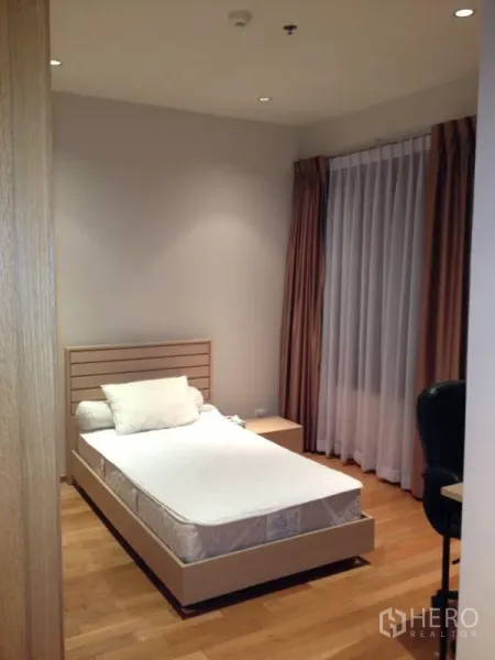 Condominium for rent or sale in Khlong Toei, Bangkok - Bedroom with a single bed, wood flooring, desk chair, and full-length curtains.