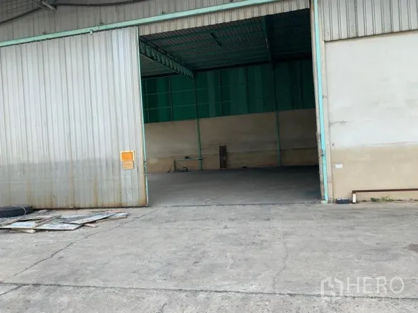 Warehouse for rent in Mueang Pathum Thani, Pathum Thani - Open warehouse entrance showing a high steel roof and spacious concrete loading area.