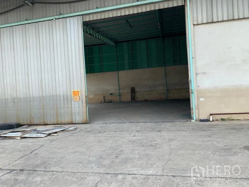 Warehouse for rent in Mueang Pathum Thani, Pathum Thani - Open warehouse entrance showing a high steel roof and spacious concrete loading area.