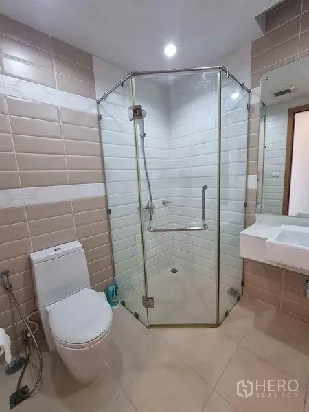 公寓 出租在Ratchathewi, Bangkok - 浴室配玻璃转角淋浴间、台上盆与座厕，米色瓷砖。