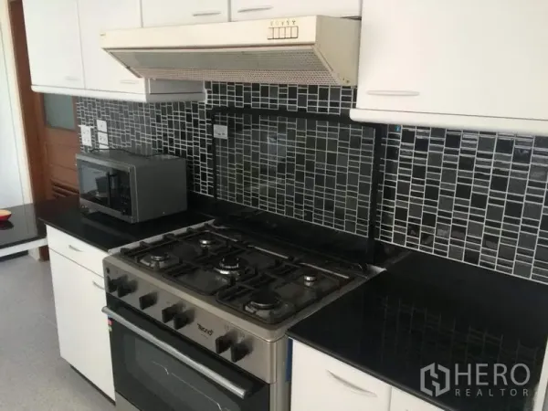 Condominium for rent in Khlong Toei, Bangkok - Fitted kitchen with gas stove, oven, range hood, black granite countertops and mosaic tile backsplash at President Park.