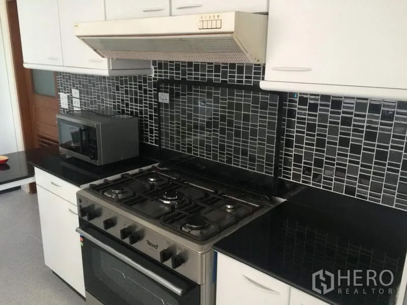 Condominium for rent in Khlong Toei, Bangkok - Fitted kitchen with gas stove, oven, range hood, black granite countertops and mosaic tile backsplash at President Park.