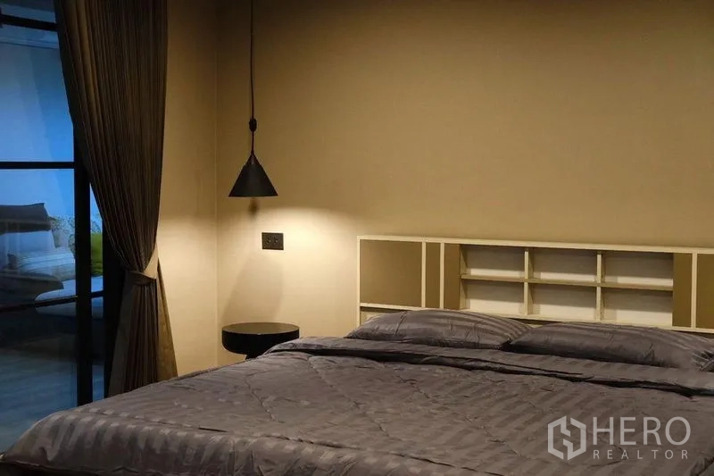 Condominium for rent in Bang Rak, Bangkok - Cozy bedroom with pendant light, built-in shelving and a large bed.