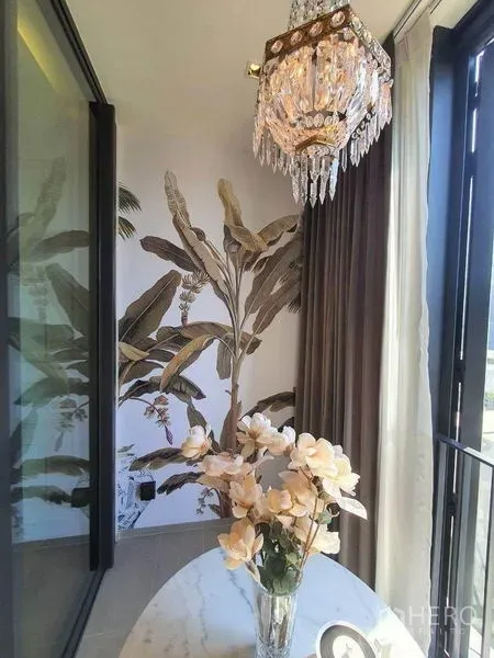 Condominium for rent in Khlong Toei, Bangkok - Bright sunroom with crystal pendant light, tropical mural and a vase on a round table.