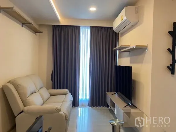 Condominium for rent in Khlong Toei, Bangkok - Cozy living area with sofa, wall-mounted shelves, TV console, and blackout curtains.