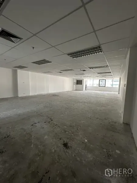 Office Space for rent in Pathum Wan, Bangkok - Open-plan office interior with grid ceiling, fluorescent light panels, bare concrete floor and large windows.