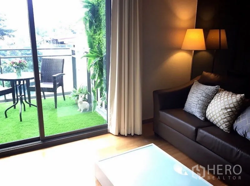 公寓 出售在Watthana, Bangkok - 客厅通向铺人造草的阳台，滑动玻璃门与户外座椅。
