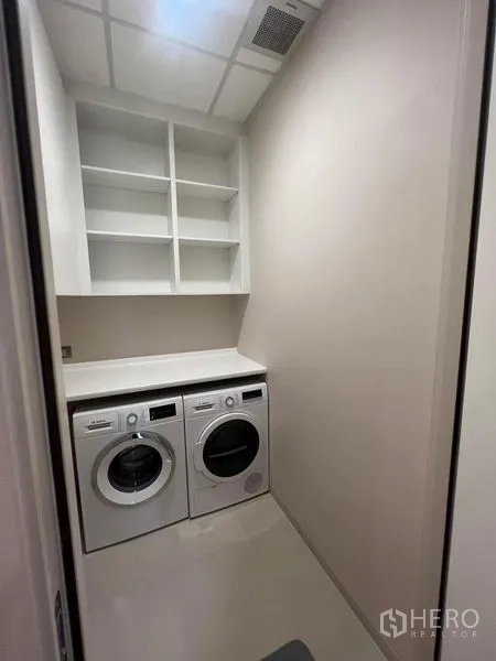 Condominium for sale - Separate laundry room with front-loading washer, dryer, countertop, and shelving.