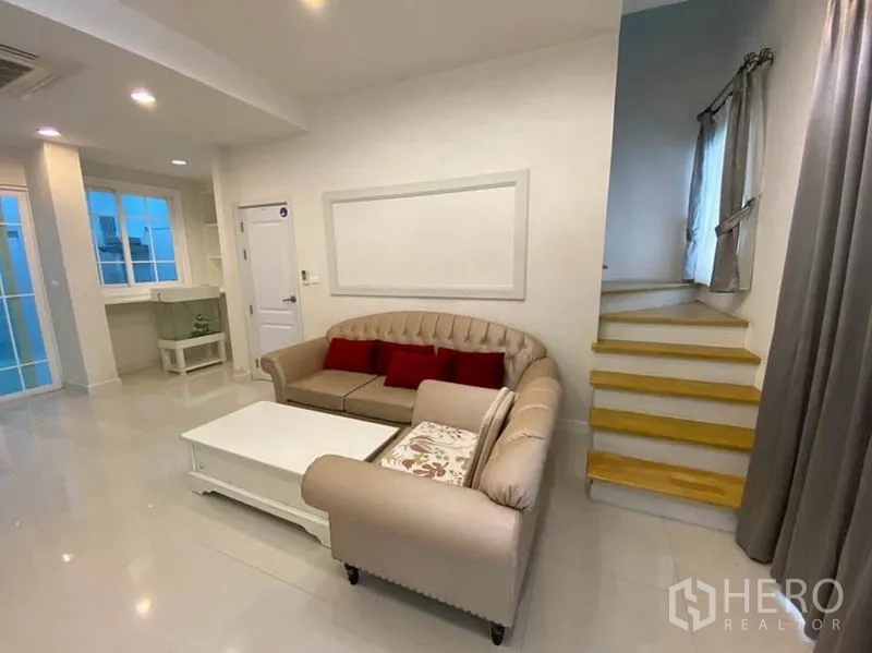 Townhouse for rent in Bang Na, Bangkok - Bright living room with sofa set, coffee table, recessed lighting, and staircase.