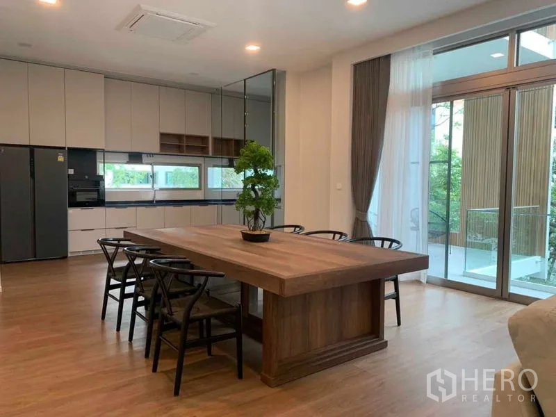 独立式住宅 出租在Saphan Sung, Bangkok - 采光充足的开放式厨房与餐区，大木餐桌、嵌入式柜体，玻璃推拉门通往露台。