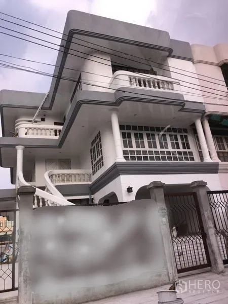带办公室的家 出租在Wang Thonglang, Bangkok - 曼谷旺通朗区三层白色家庭办公楼，设宽阳台、柱式立面、外部旋转楼梯与带门庭院。