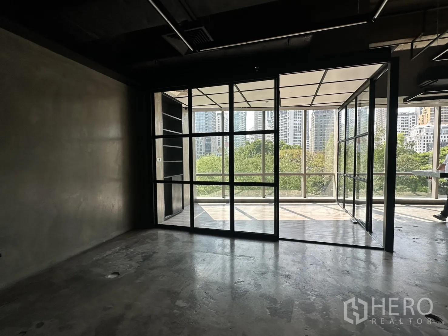 ออฟฟิศ for rent in Pathum Wan, Bangkok - ห้องว่างมองออกไปยังประตูกระจกกรอบดำพร้อมวิวเมืองเหนือแนวต้นไม้