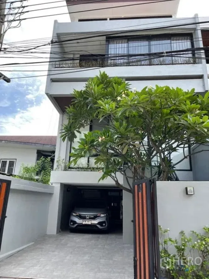 Townhouse for rent in Khlong Toei, Bangkok - Modern Ekkamai townhouse exterior with gated carport and mature tree.