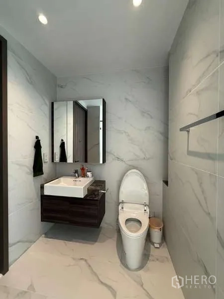 Condominium for rent or sale in Sathon, Bangkok - Contemporary bathroom with wall-hung vanity, mirror cabinet and marble-look tiles.