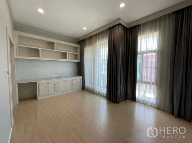 Townhouse for sale - Sunlit bedroom corner with built-in shelves, desk, and tall windows with double curtains.