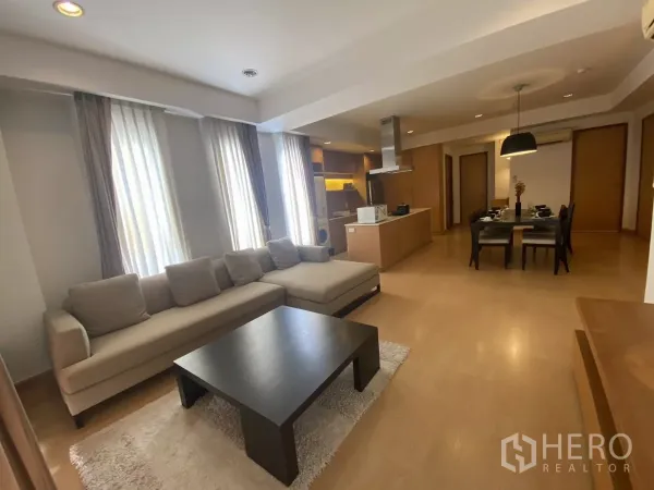 公寓 出租在Watthana, Bangkok - 开放式客厅，L 形沙发、茶几与落地窗帘，曼谷公寓内景。