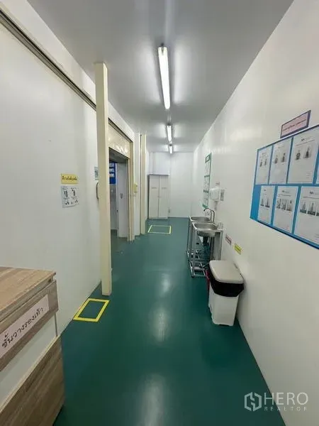 Warehouse for rent or sale in Lam Luk Ka, Pathum Thani - Clean, well‑lit corridor with sink, safety posters and green epoxy flooring.