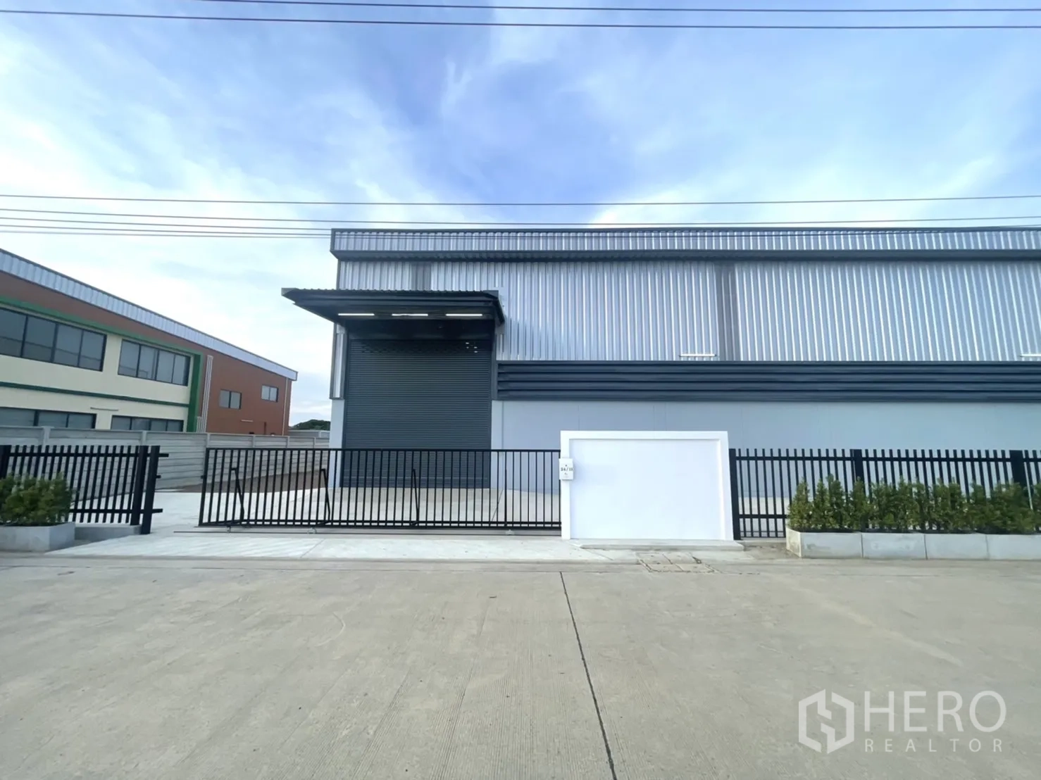 Factory for rent or sale in Bang Yai, Nonthaburi - Street frontage showing loading bay shutter and secure black fence.