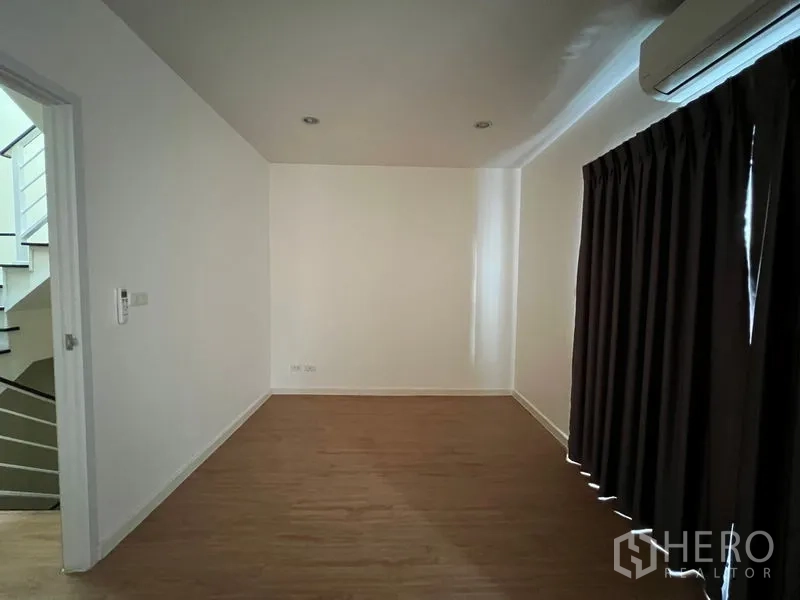 Townhouse for rent in Bang Kapi, Bangkok - Empty upstairs room with wood floor and dark curtains beside staircase.