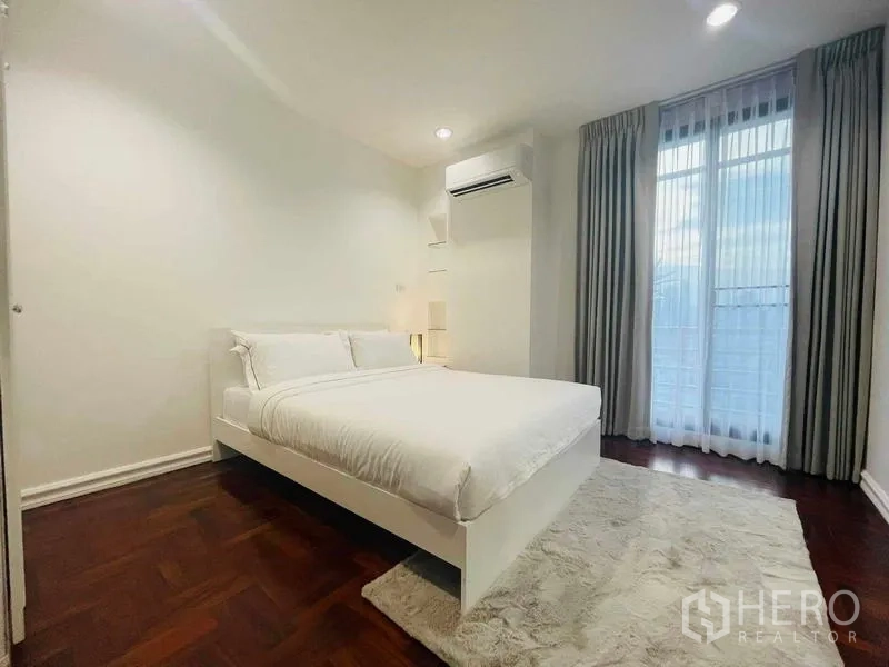 Condominium for rent - Cozy bedroom with white bed, rug, and tall window with curtains.