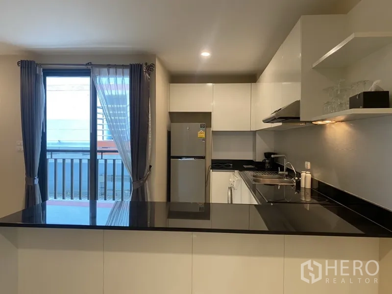 Condominium for rent in Watthana, Bangkok - Modern kitchen with black stone countertops, white cabinetry, and window by the balcony.