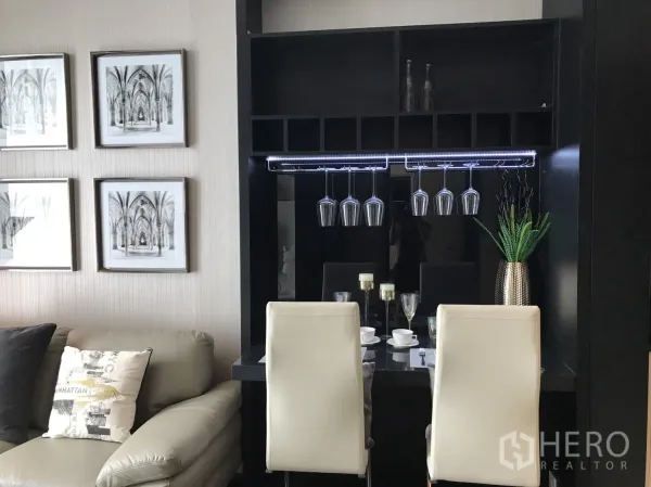 Condominium for rent or sale in Watthana, Bangkok - Cozy dining bar with hanging wine glasses, white chairs and wall art beside a sofa in a modern condo living area.
