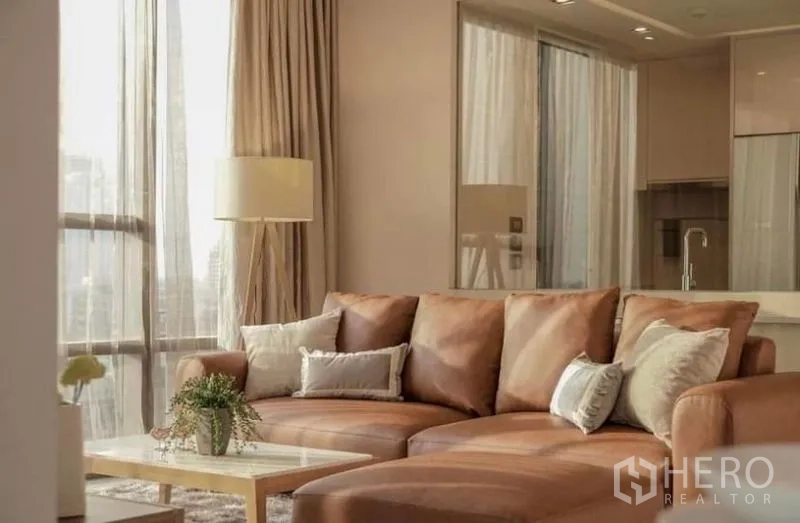 คอนโด ให้เช่าในSathon, Bangkok - โซฟาหนังสีน้ำตาลพร้อมหมอนอิงและโคมไฟยืน โดยมีครัวโมเดิร์นด้านหลัง