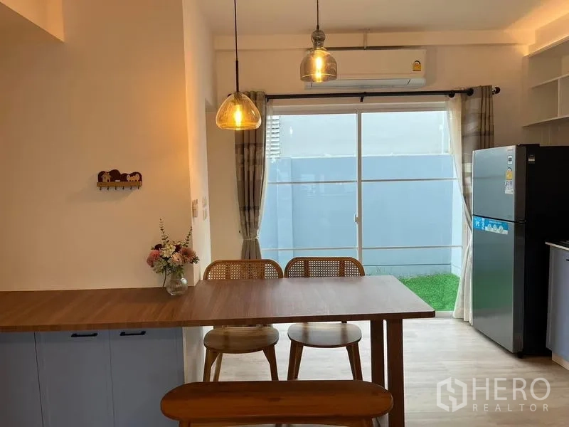 Townhouse for rent in Prawet, Bangkok - Dining area with pendant lights and sliding glass doors opening to a small private yard.