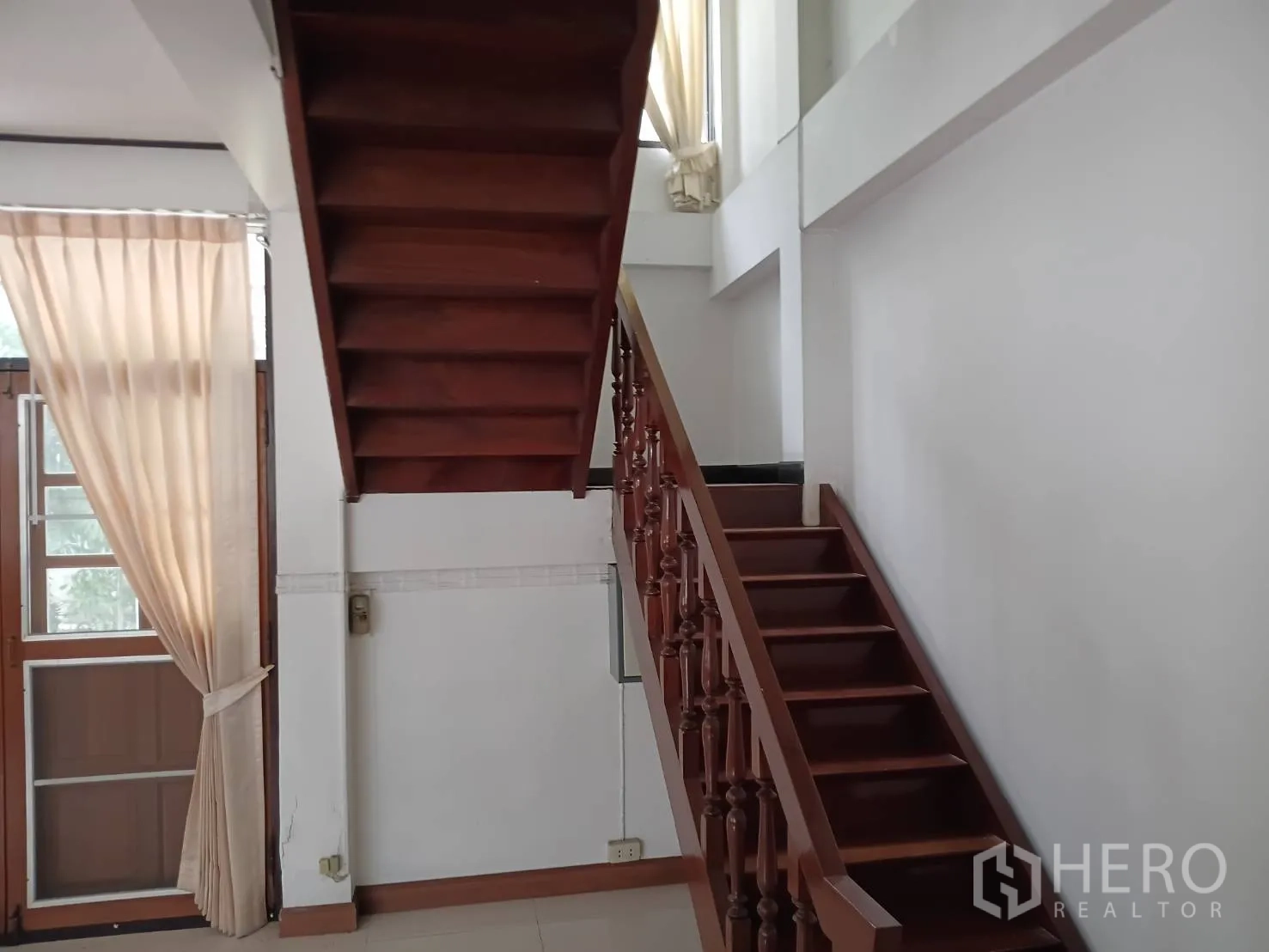 独栋房屋 for sale in Watthana, Bangkok - 木质楼梯与扶手，旁有高窗与窗帘。