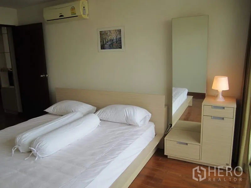 公寓 出租在Bang Rak, Bangkok - 客卧铺白色床品，床头柜与台灯、全身镜及空调。